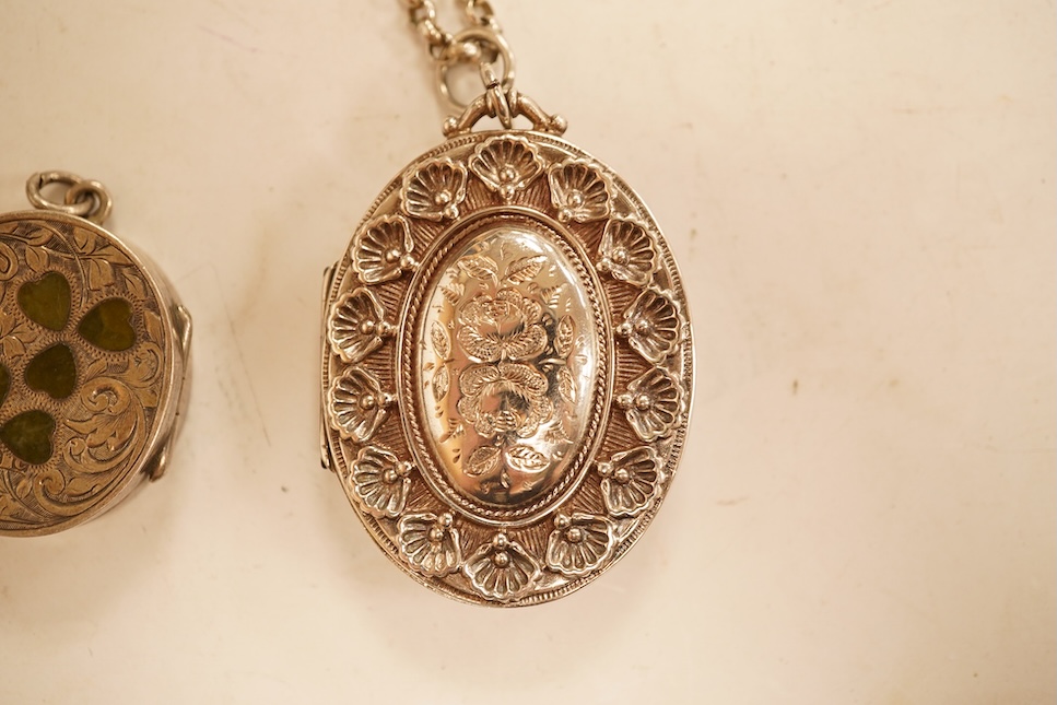 A late Victorian embossed and engraved oval silver locket, 42mm, on a later white meta belcher link chain, together with an Edwardian silver and hardstone inlaid pill box, now with pendant mount.